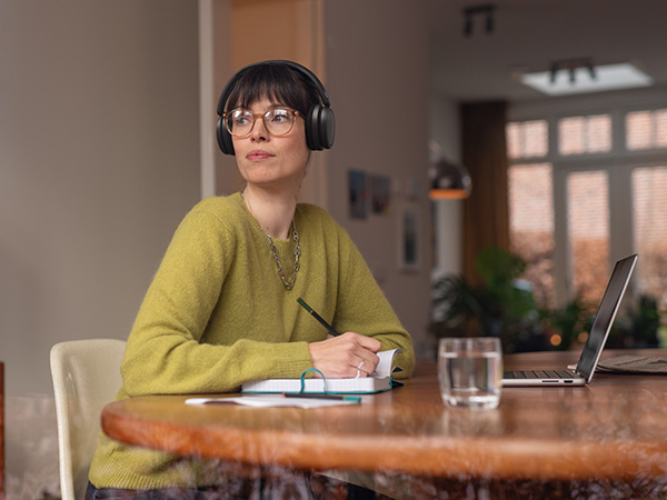 A person wearing comfortable Philips headphones sits at a table with a notebook and laptop