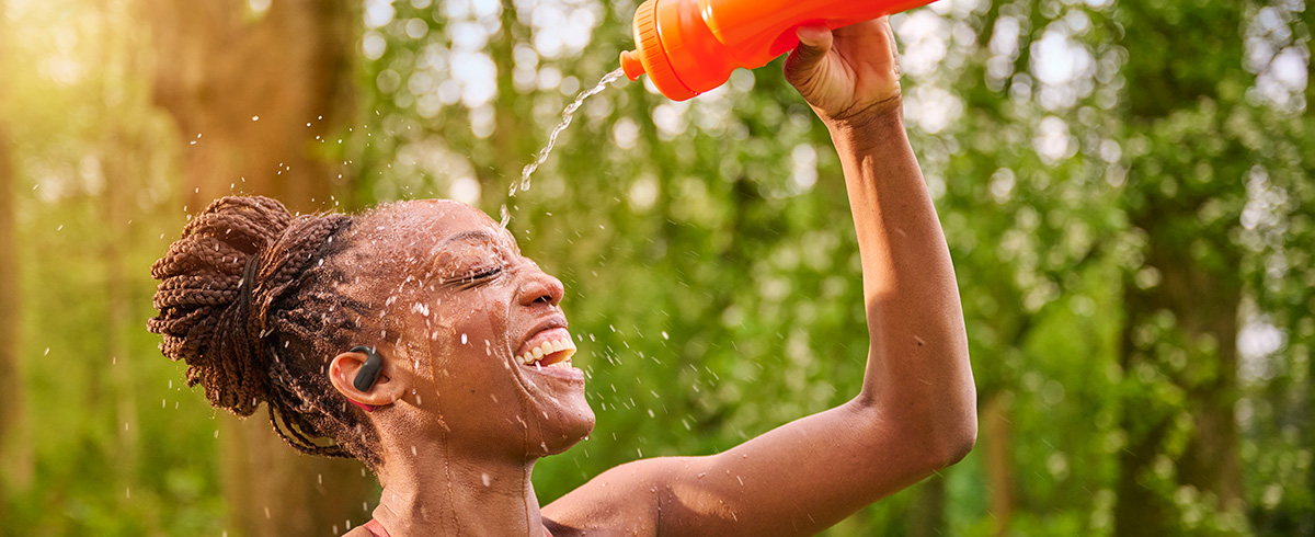 Woman cooling off by pouring water over her head while wearing Philips sports headphones outdoors